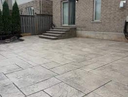 Gray stamped slate patio next to a brick home